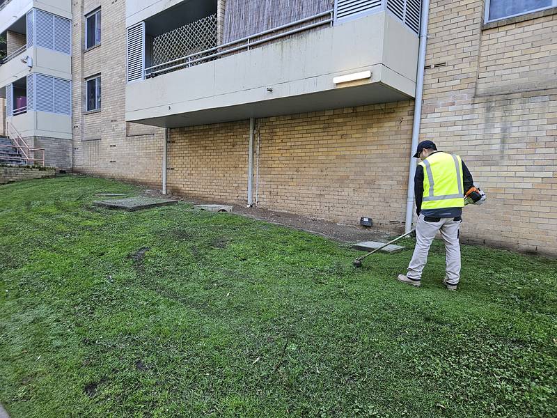 Crew member edging along a unit block wall with a brushcutter